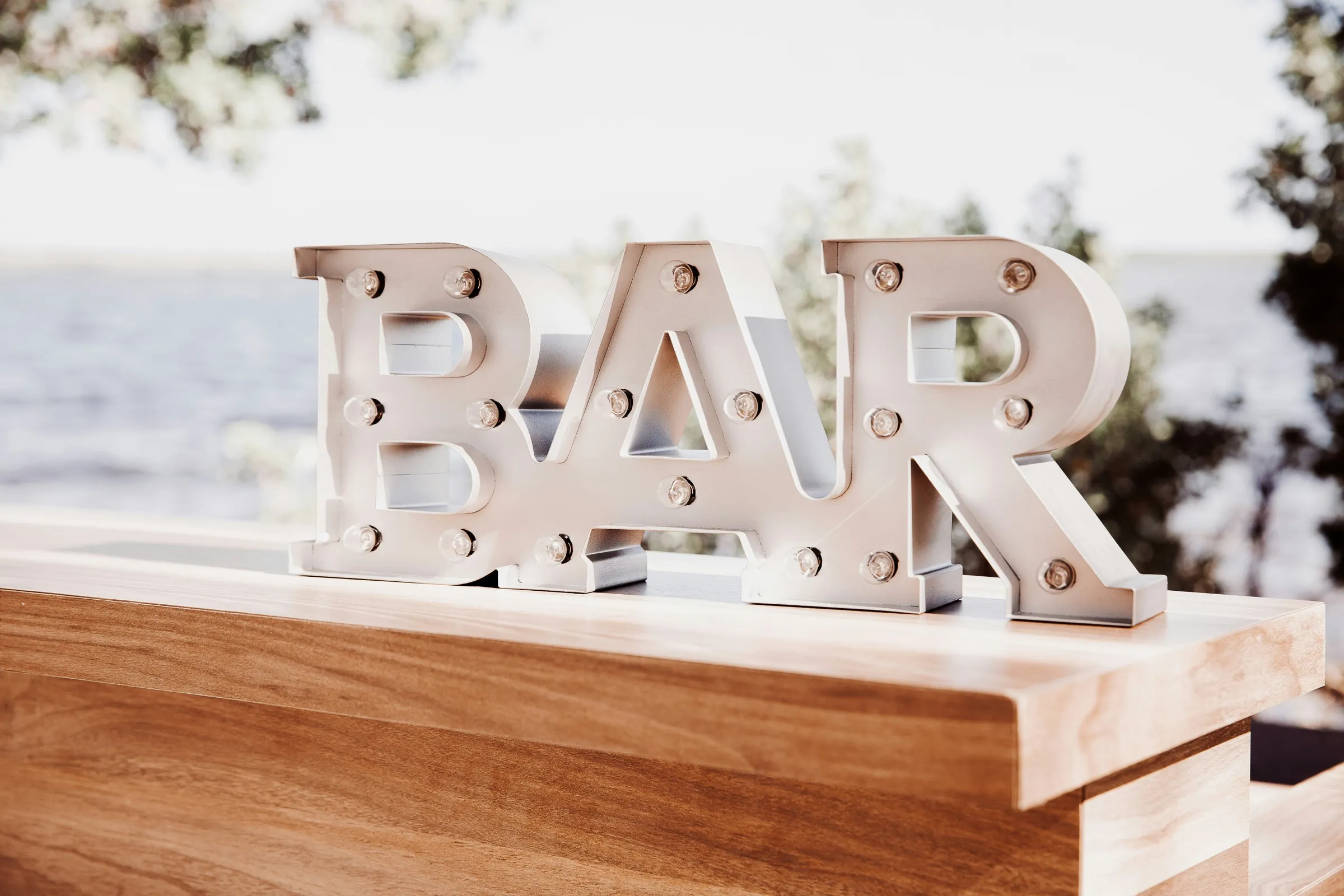 Freistehende weiße Buchstaben „Bar“ auf einem Holztresen im Freien