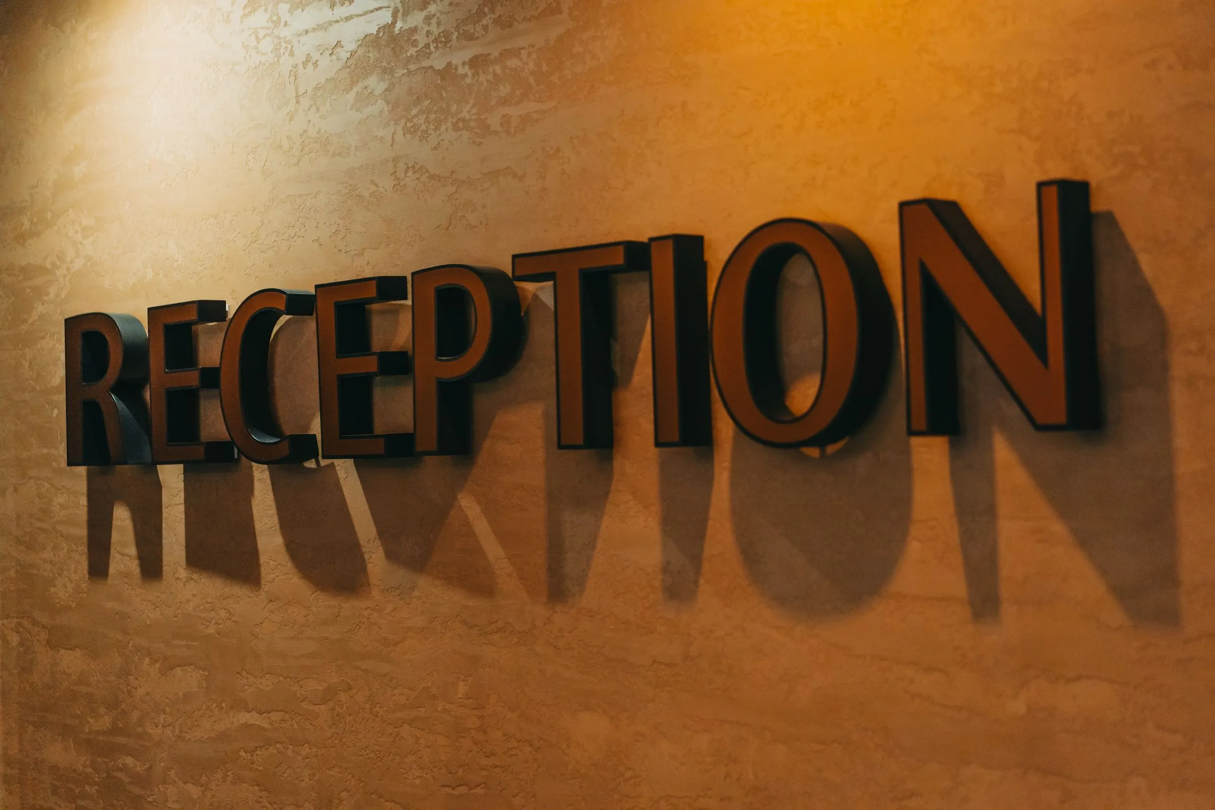 3D-Buchstaben „Reception“ an einer warm beleuchteten Wand mit Schattenwurf