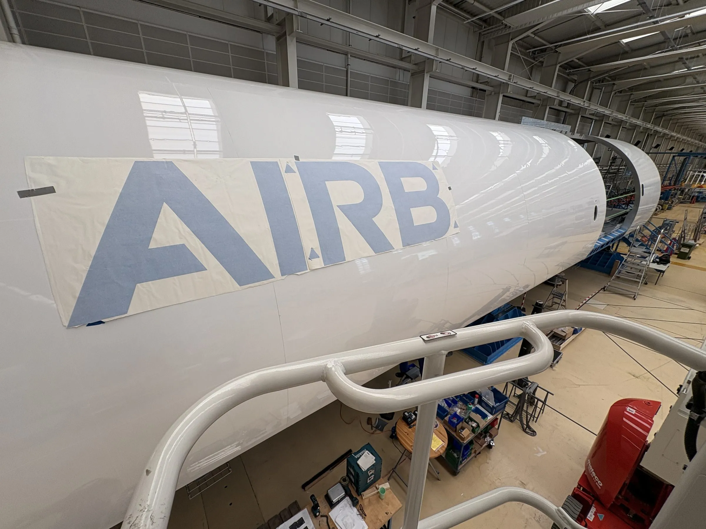 Airbus-Schriftzug mit Übertragungsfolie auf einem Rumpfsegment, von der Hebebühne aus gesehen