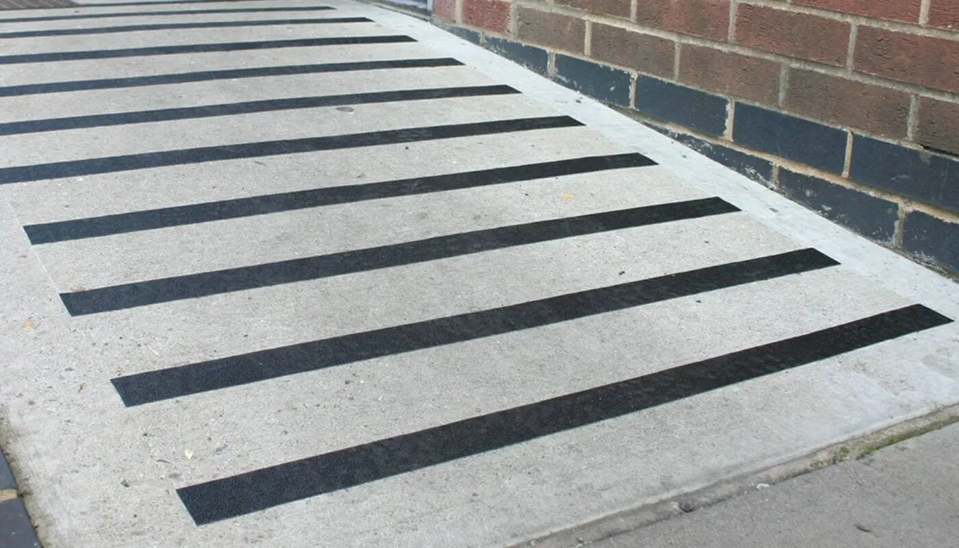 Betonrampe an einer Klinkerwand mit quer verlegten schwarzen Antirutschstreifen
