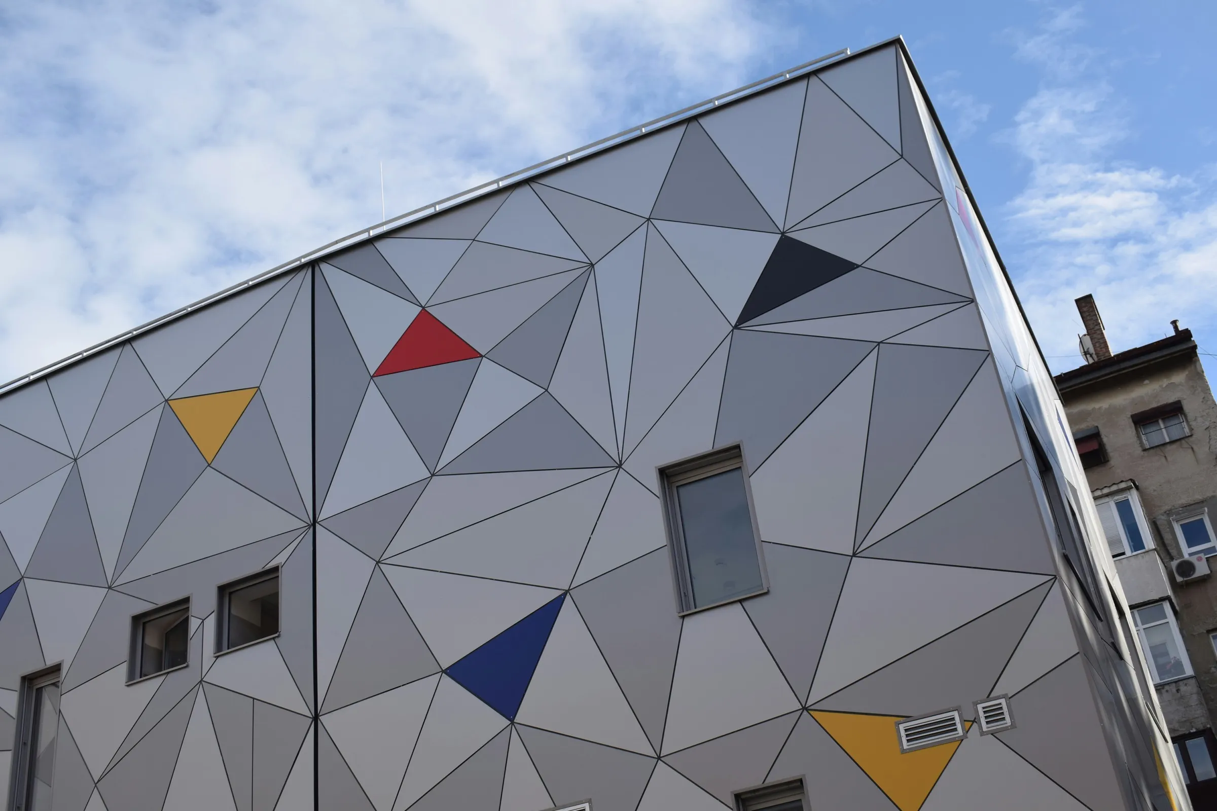 Hausfassade mit grafischem Muster aus grauen, roten, gelben und blauen Dreiecken