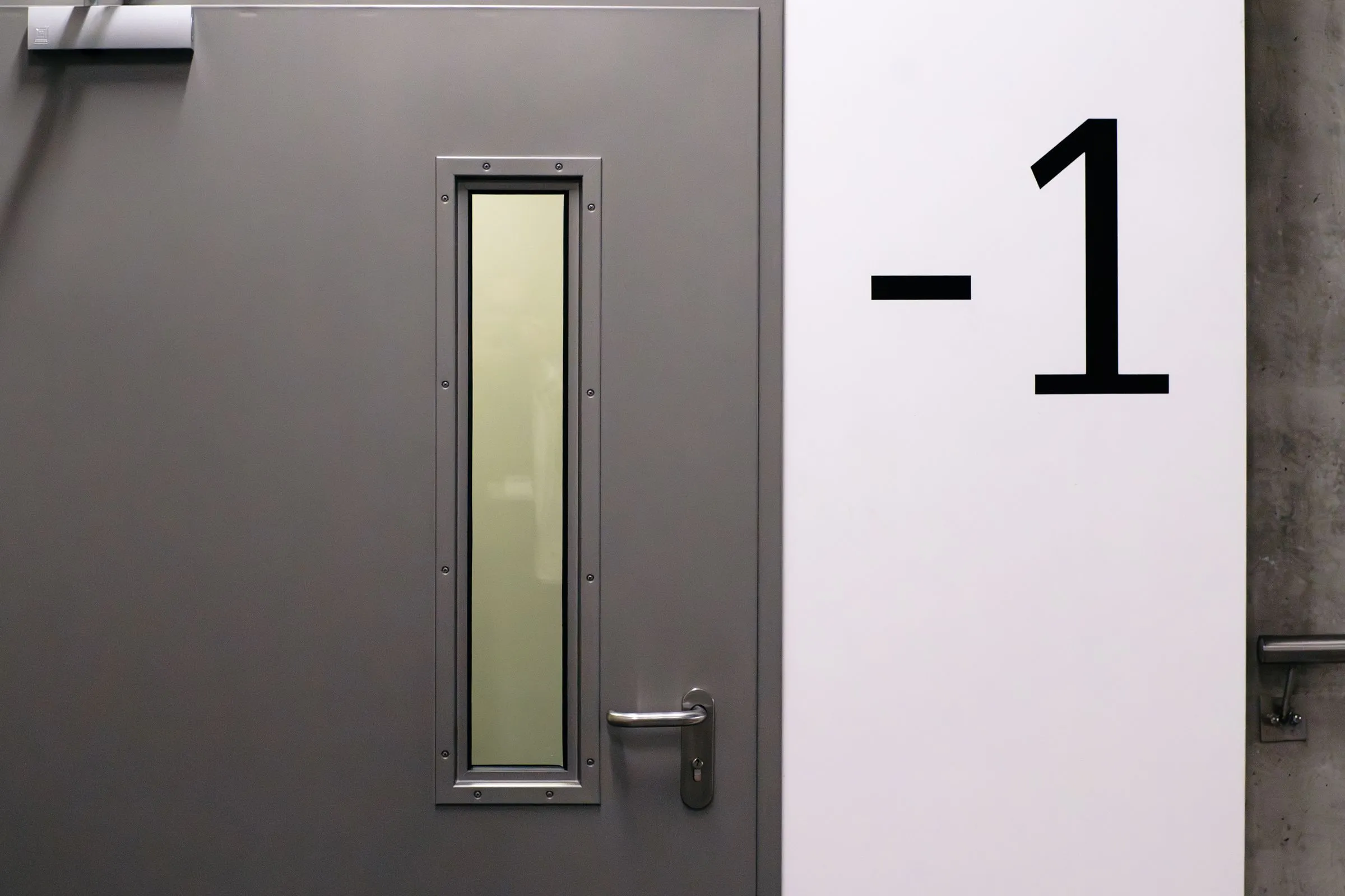 Graue Stahltür mit großer Etagennummer -1 an der Wand daneben