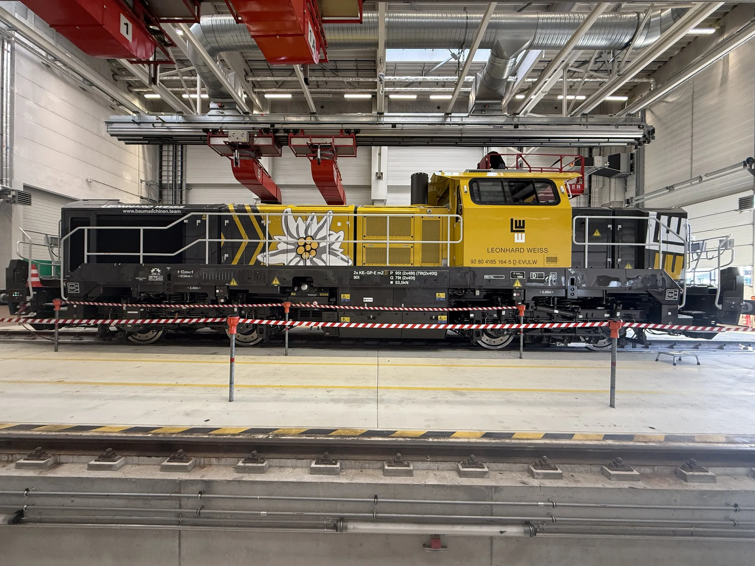Gelb-schwarze Lokomotive von Leonhard Weiss mit Logo und Edelweiß-Dekor in einer hellen Werkhalle