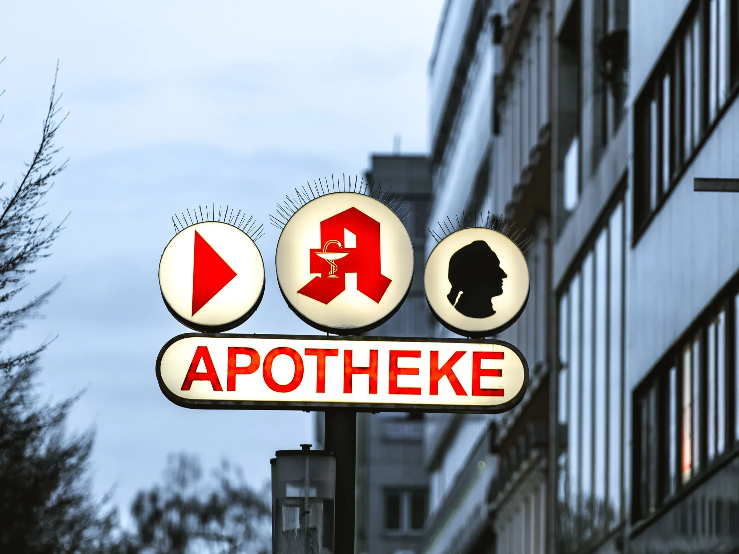 Beleuchtetes Apothekenschild mit rotem Apotheken-A und Schriftzug in der Abenddämmerung