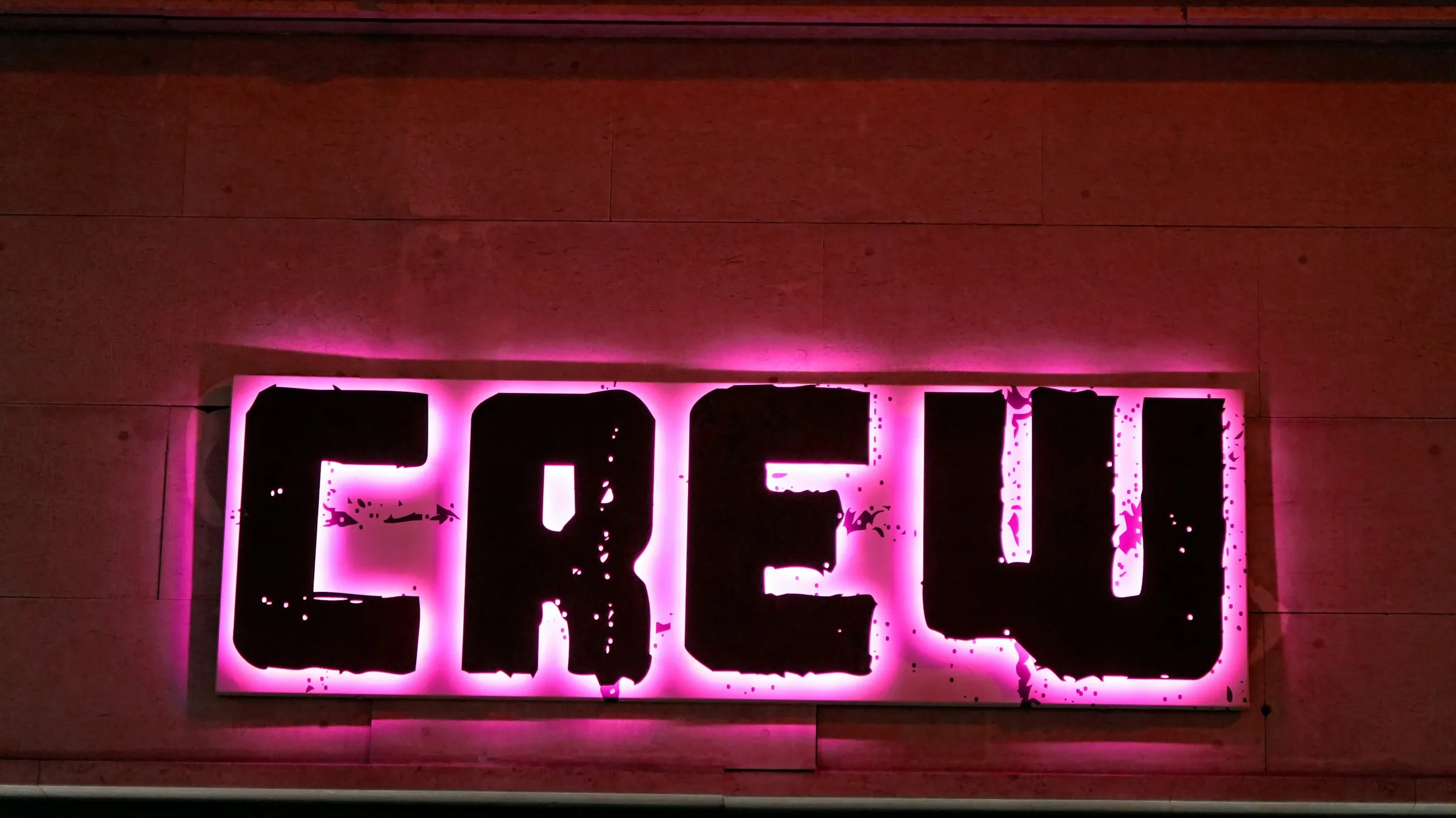 Schriftzug mit pinkfarbenem Lichtkranz an einer rötlichen Wand