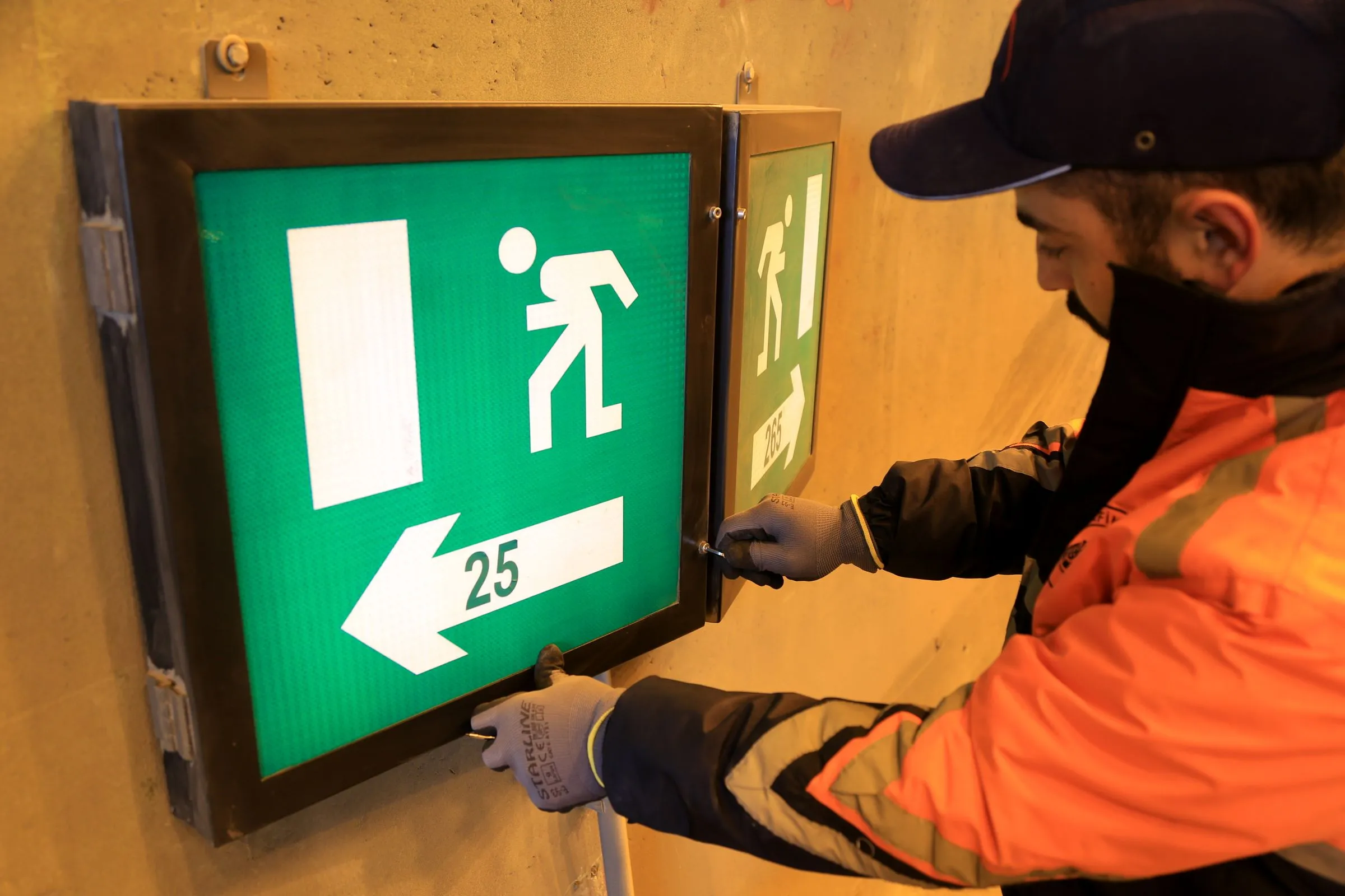 Techniker arbeitet an einem beleuchteten Hinweisschild an einer Tunnelwand