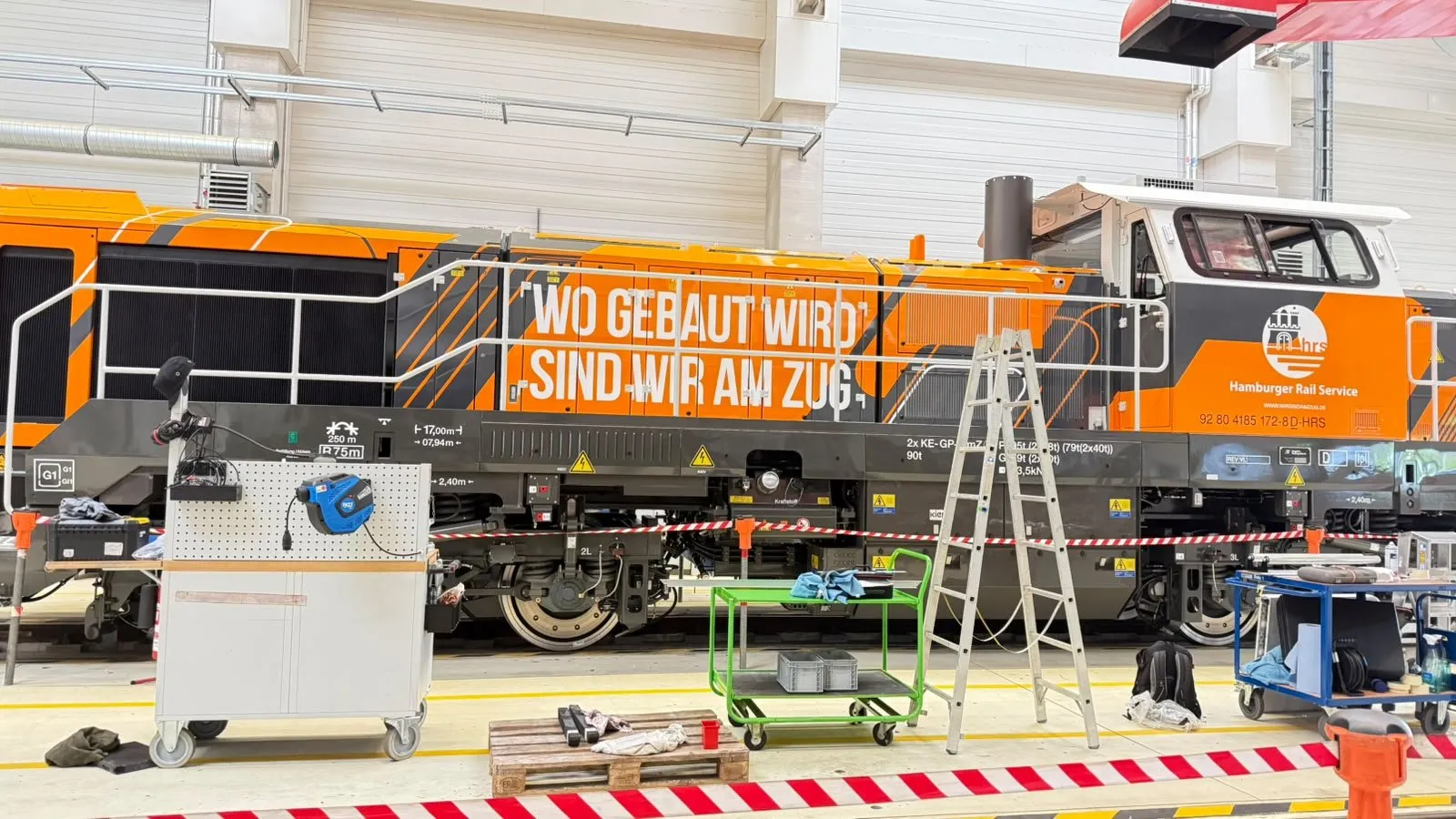 Vollfolierte Lokomotive des Hamburger Rail Service mit dem Slogan Wo gebaut wird sind wir am Zug in einer Werkhalle