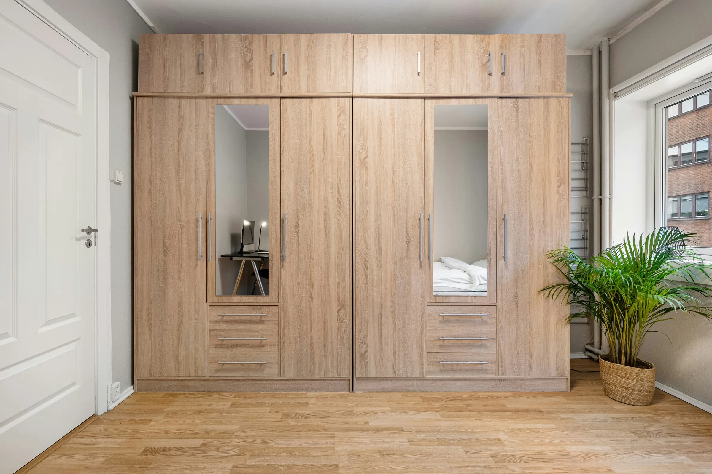 Großer Kleiderschrank in Holzoptik mit Spiegeltüren neben einer weißen Zimmertür