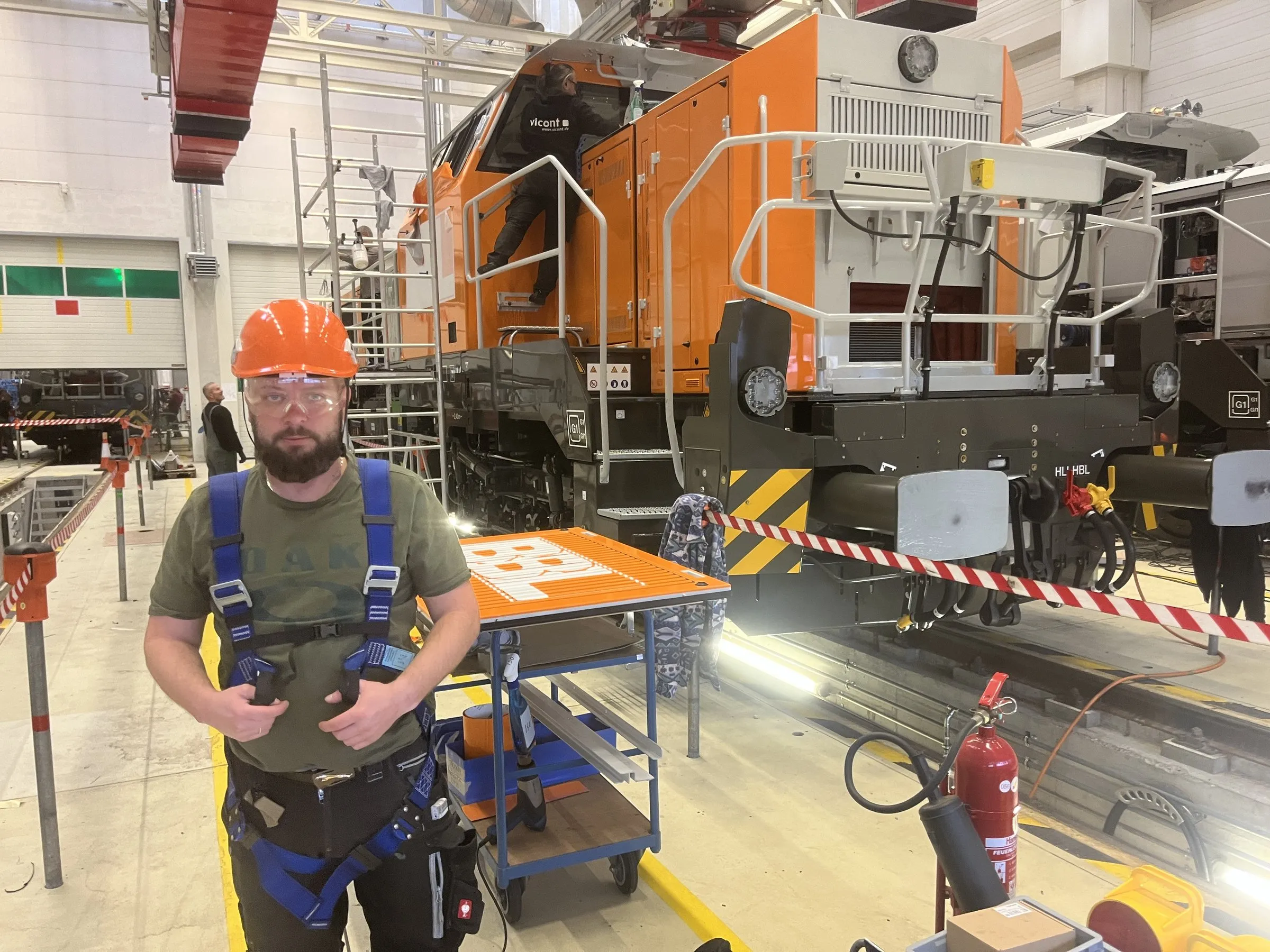 Monteur mit Helm und Auffanggurt vor einer orange folierten Lokomotive