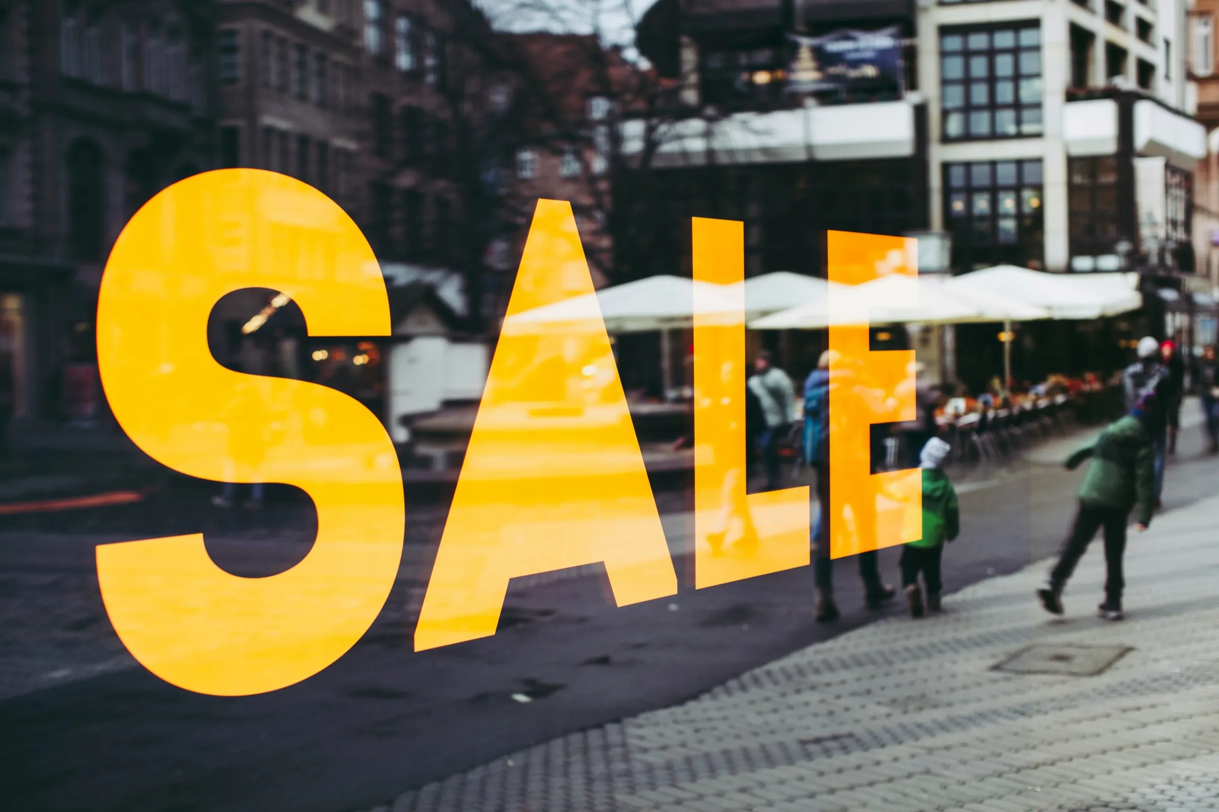 Gelber SALE-Schriftzug auf einem Schaufenster, dahinter eine Fußgängerzone