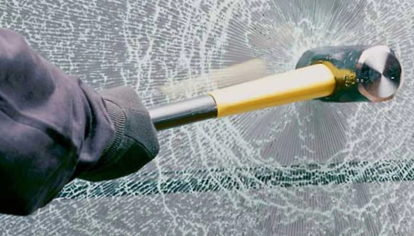 Hammer trifft auf eine Glasscheibe, das Glas reißt, bleibt aber zusammen