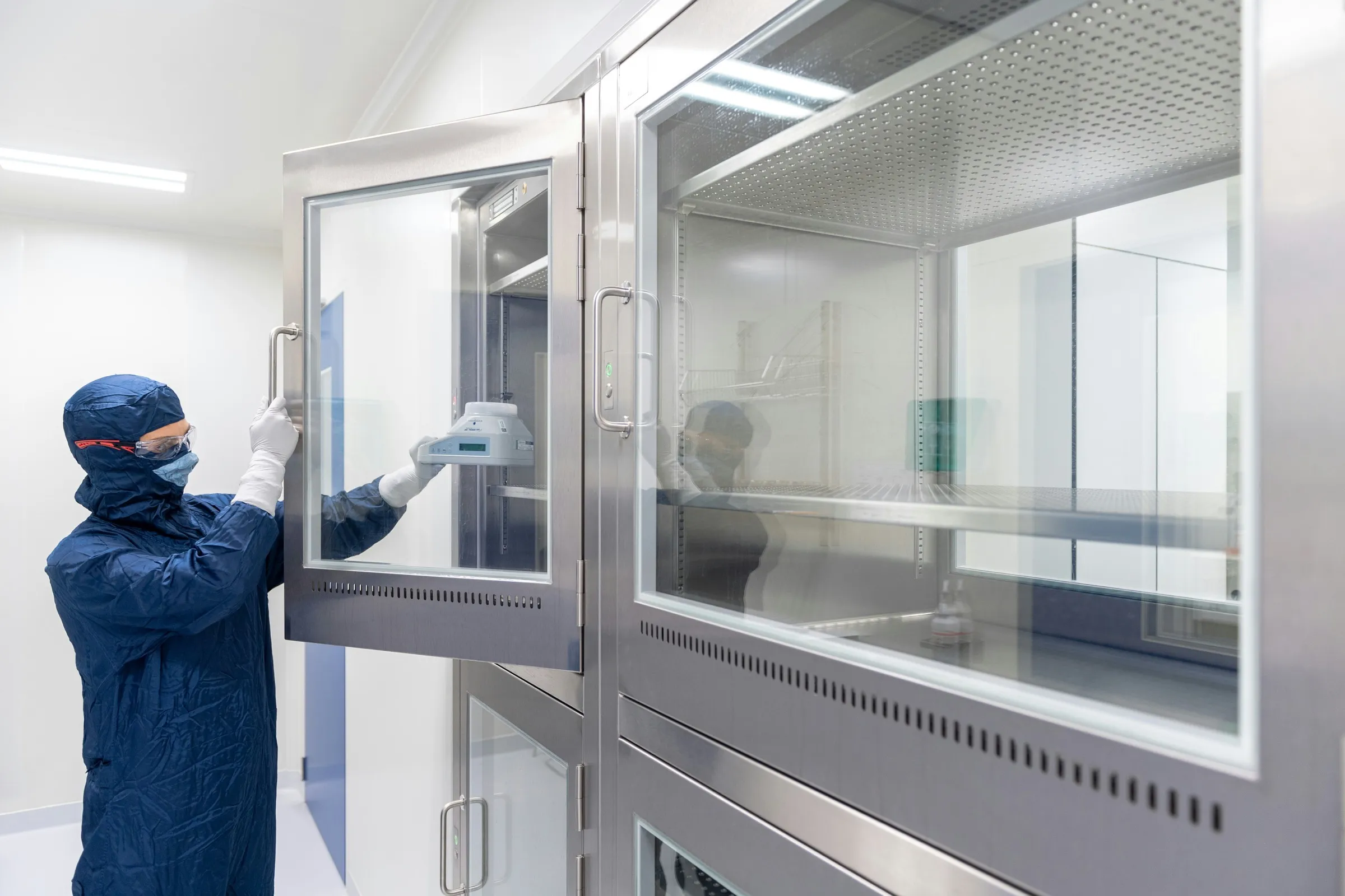 Person in Schutzanzug öffnet einen Glasschrank im Labor