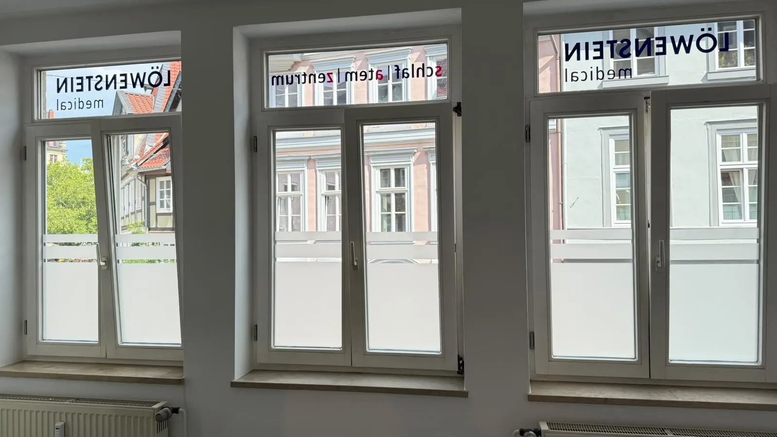 Fenster einer medizinischen Praxis mit Milchglas-Sichtschutzstreifen und Logo-Beschriftung im Oberlicht
