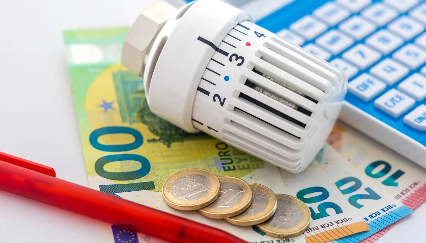 Heizkörperthermostat auf Euroscheinen und Münzen neben einem Taschenrechner