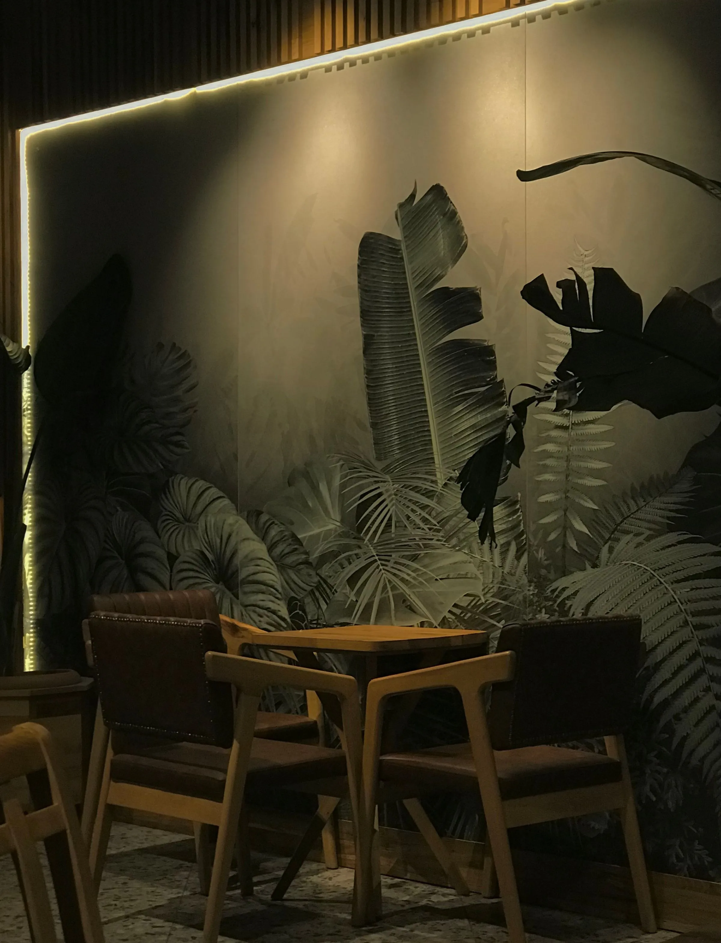 Sitzecke in einem Café vor einem dunklen Wandbild mit großen Blättern