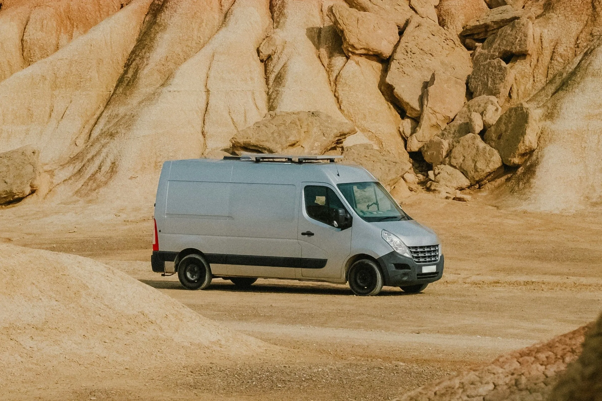 Silberner Kastenwagen-Camper mit Dachträger vor hellen Sandsteinfelsen, Front schräg von vorn
